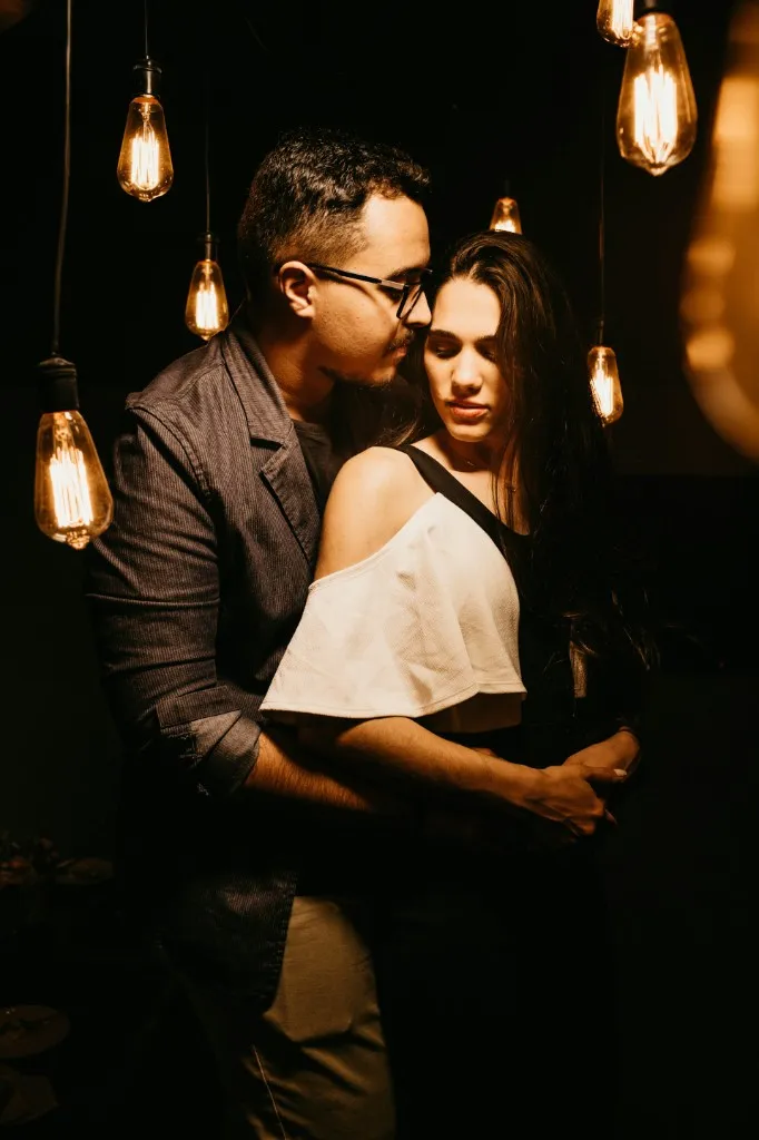 Couple embracing under warm Edison bulb lights — perfect for a date night